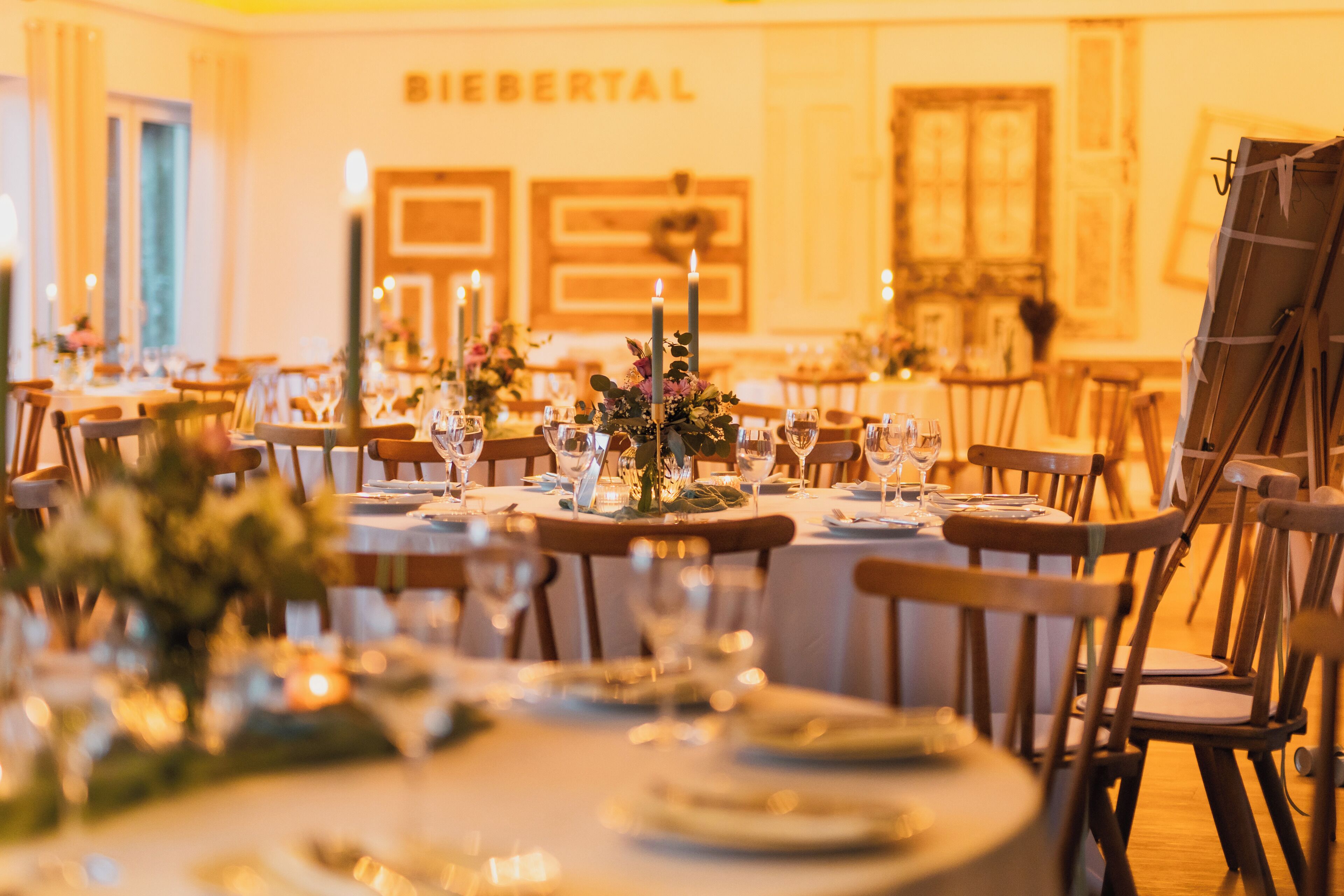 Ein Essbereich mit runden Tischen, Kerzen und Blumenarrangements.
