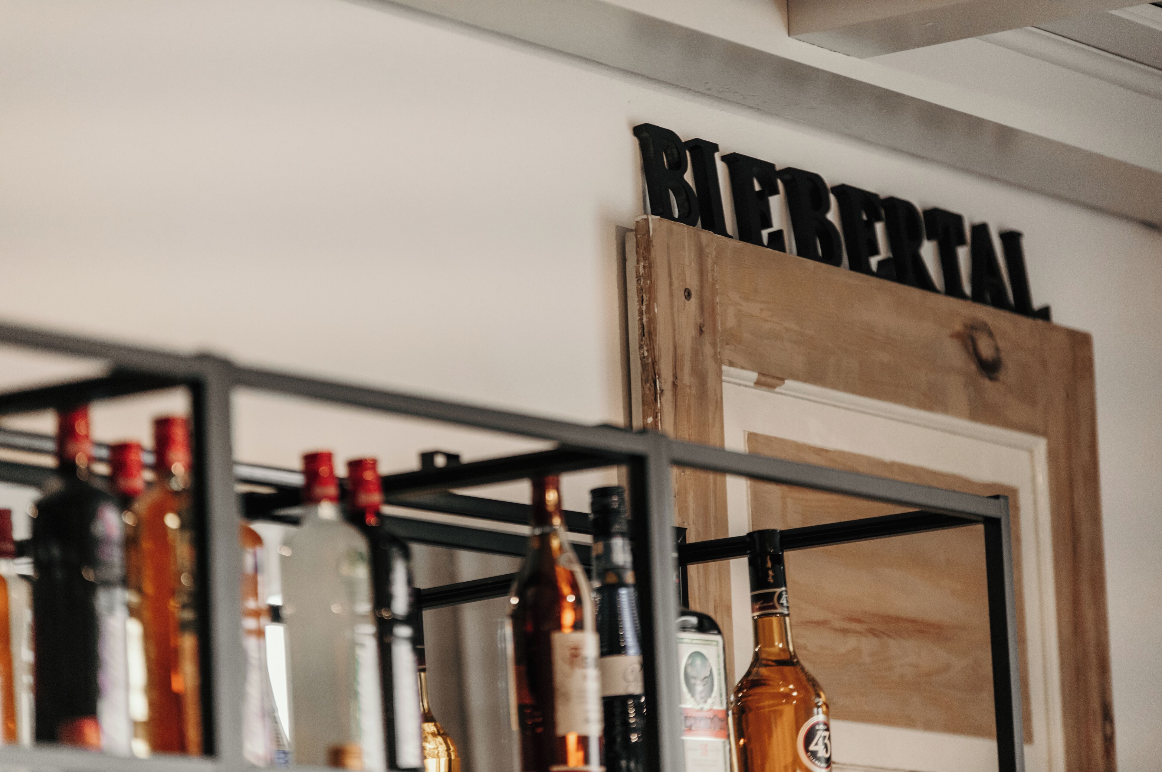 A bar area with a wooden sign reading "RIEBERTAL" and various bottles of alcohol on shelves.