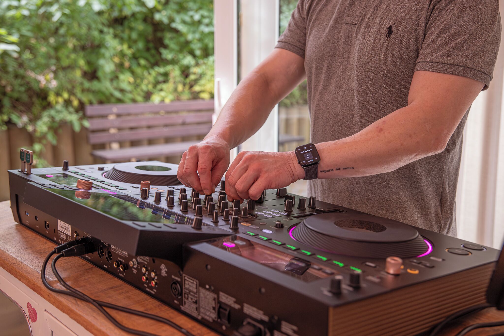 Una persona usando un mezclador de DJ con varias perillas y botones, conectado a una computadora.
