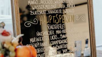 A framed menu listing various dishes and beverages, including items like 'Ochsenschwein Herztomate' and 'Mango...Avocado...Wildkraut'.