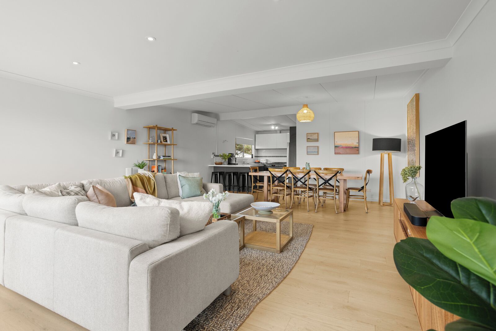 A modern living room with a grey sofa, wooden dining table, and a kitchen in the background.