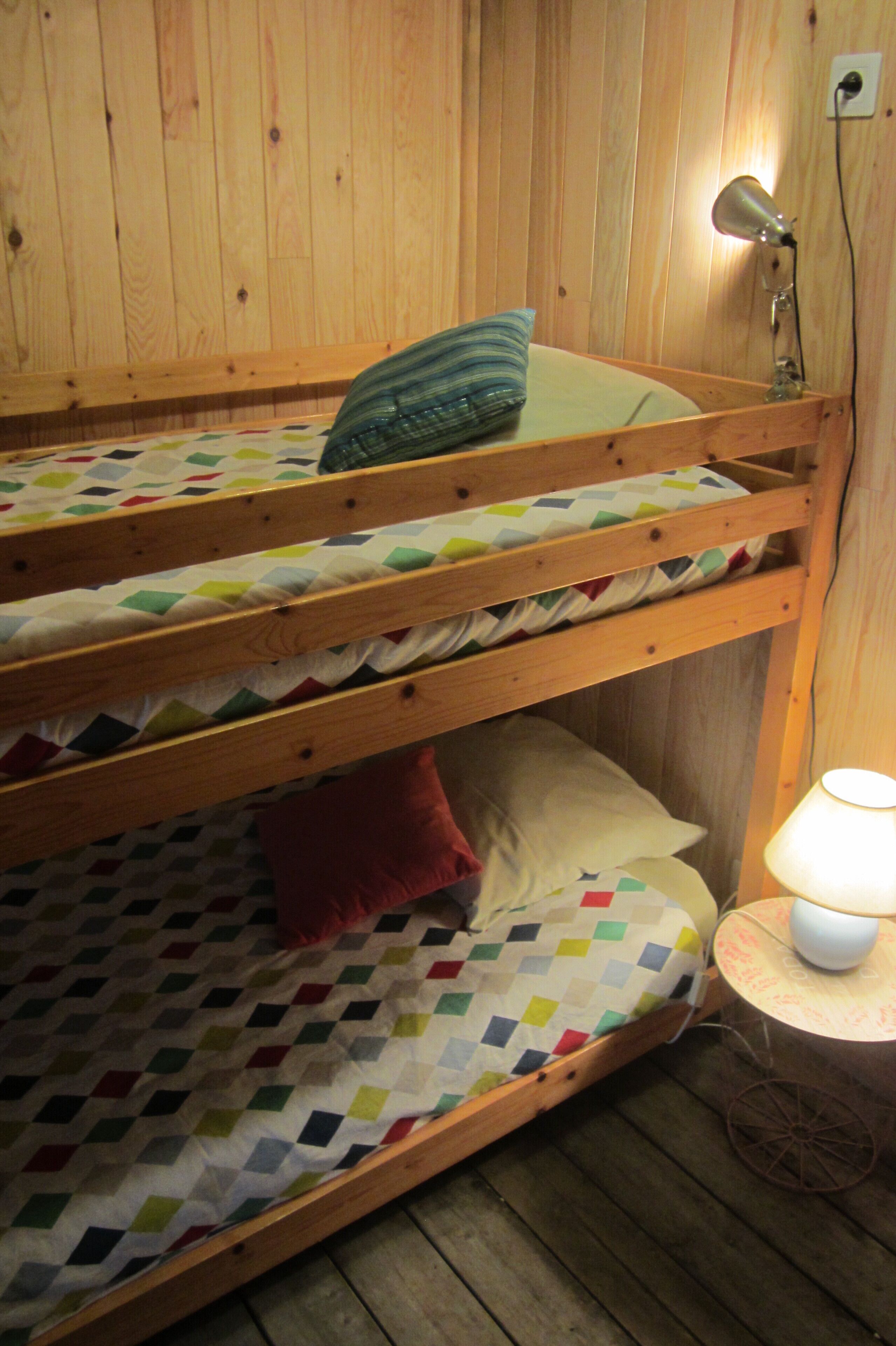 Ein Stockbett mit einer gesteppten Matratze, einem Kissen und einer Nachttischlampe auf Holzdielen.