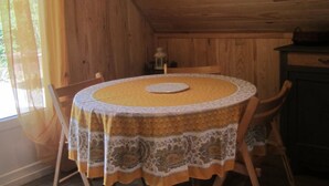 Een houten eettafel met een tafelkleed met patroon, omringd door houten stoelen, in een kamer met houten wanden en een schuine kap.