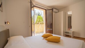 A bedroom with a bed, two pillows, a nightstand, a mirror, and a sliding door leading to an outdoor area. - Pater Meus Suites (Cefalù)