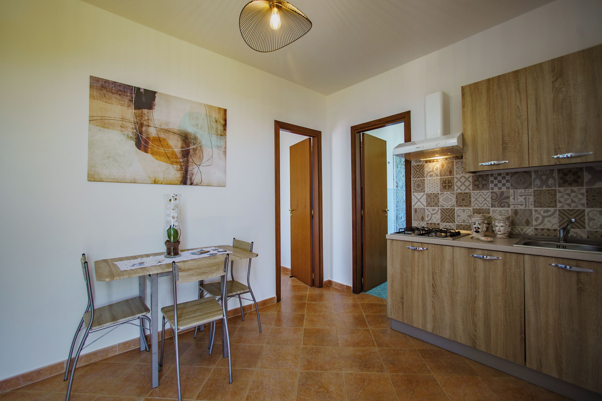Cozinha moderna com área de jantar, destacando uma mesa com cadeiras, luminária pendente e ladrilhos estampados.