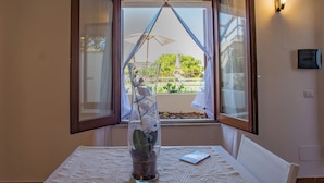 A room with a table, a vase with flowers, and a window with curtains. - Pater Meus Suites (Cefalù)