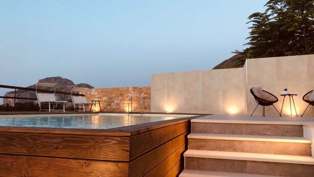 A pool area with steps leading up to a seating area with chairs and a table. - Pater Meus Suites (Cefalù)