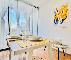 Un comedor con una mesa preparada para cuatro, un vaso de agua y una obra de arte enmarcada en la pared.