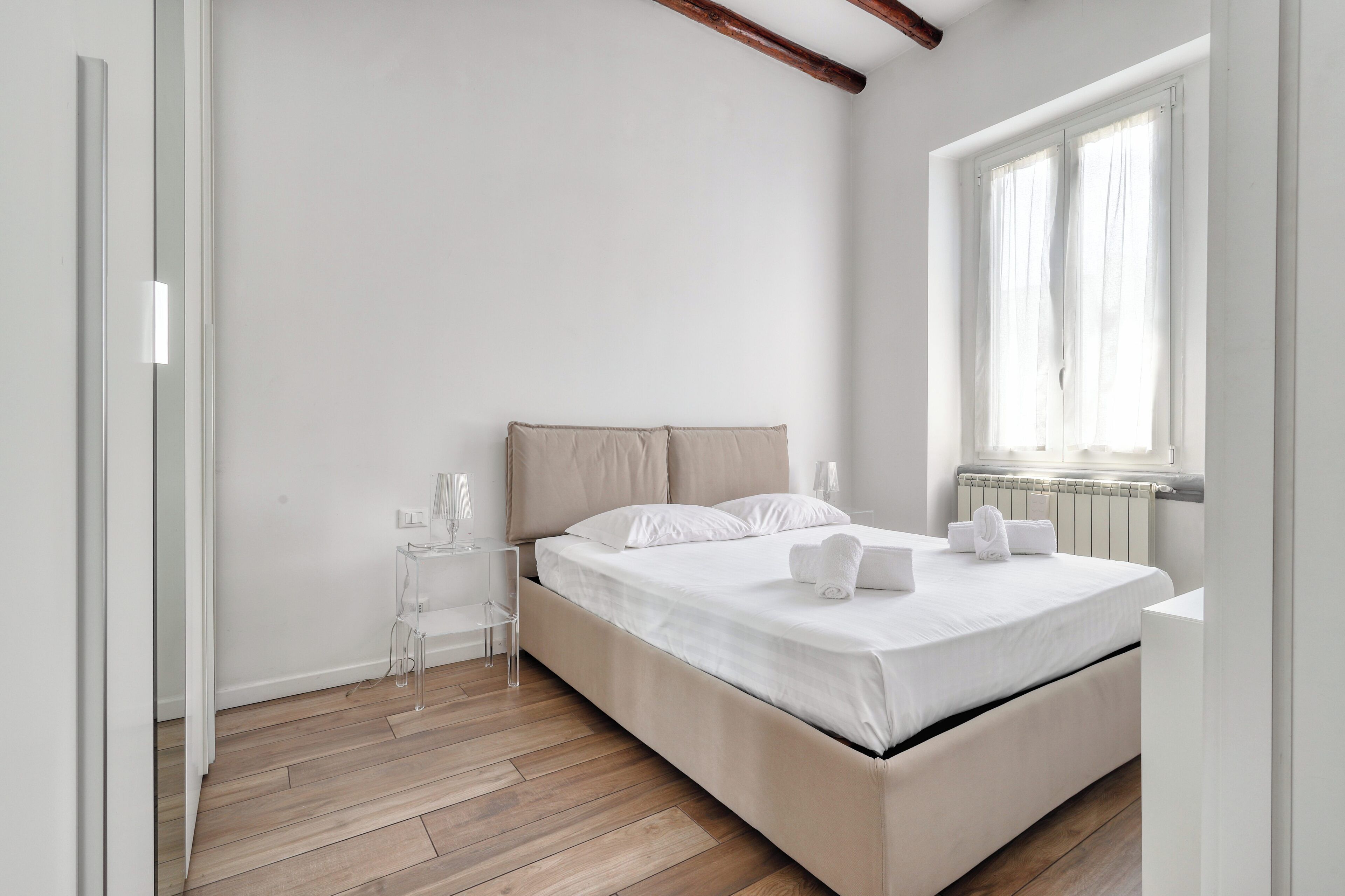 Een minimalistisch ingerichte slaapkamer met een bed, een raam en een radiator.