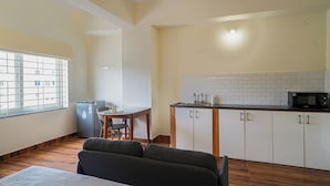 Ein kompaktes Hotelzimmer mit Küchenzeile, Essbereich und großem Fenster.