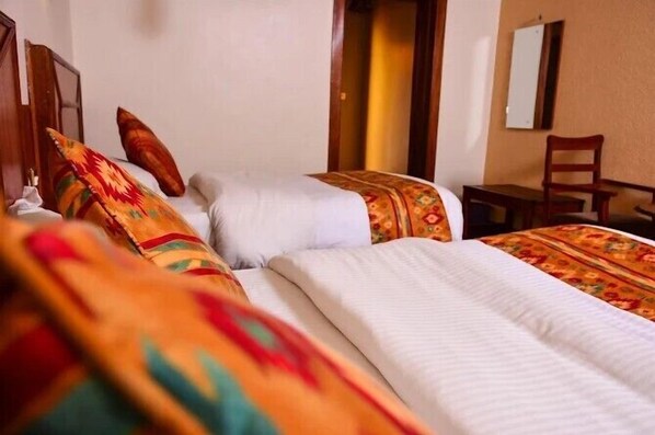 A hotel room with two beds, each with patterned bedding and a wooden headboard.
