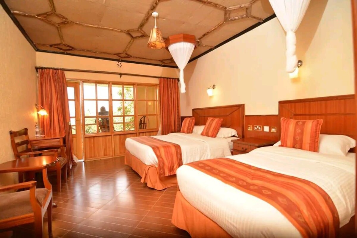 A hotel room with two beds, wooden furniture, a large window, and a unique ceiling design.