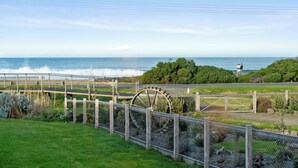 Un paisaje costero con una noria grande, un puente de madera y un faro a lo lejos.
