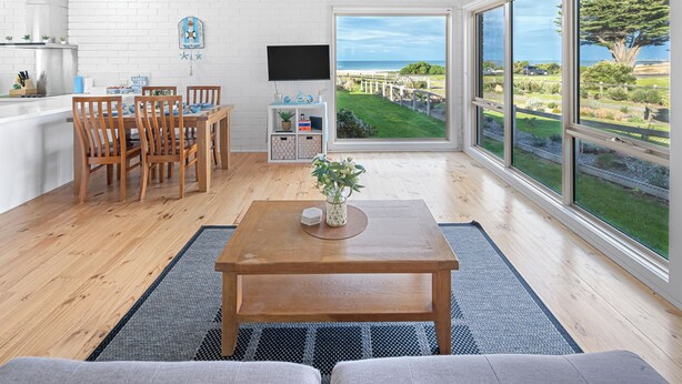 Una sala de estar moderna con una mesa de centro de madera, un televisor montado en la pared y un amplio ventanal con vistas al exterior.