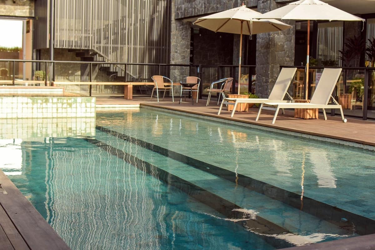 A swimming pool with lounge chairs and umbrellas, surrounded by a stone wall and modern architecture.