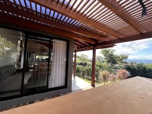 Un espacio al aire libre techado con vistas a una cocina y zona de comedor, vigas de madera en el techo y una mesa.