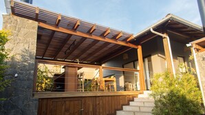 Een modern huis met een houten terras, stenen muren en een trap naar een overdekte veranda.