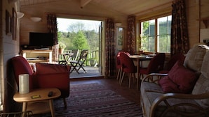 A cozy cabin interior with a wooden ceiling, a television, a dining area with chairs, and a sofa. - Tucked Away Log Cabin on Welsh Hill Farm (Sennybridge)