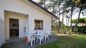 Une maison moderne avec un patio, des chaises blanches et une petite table.