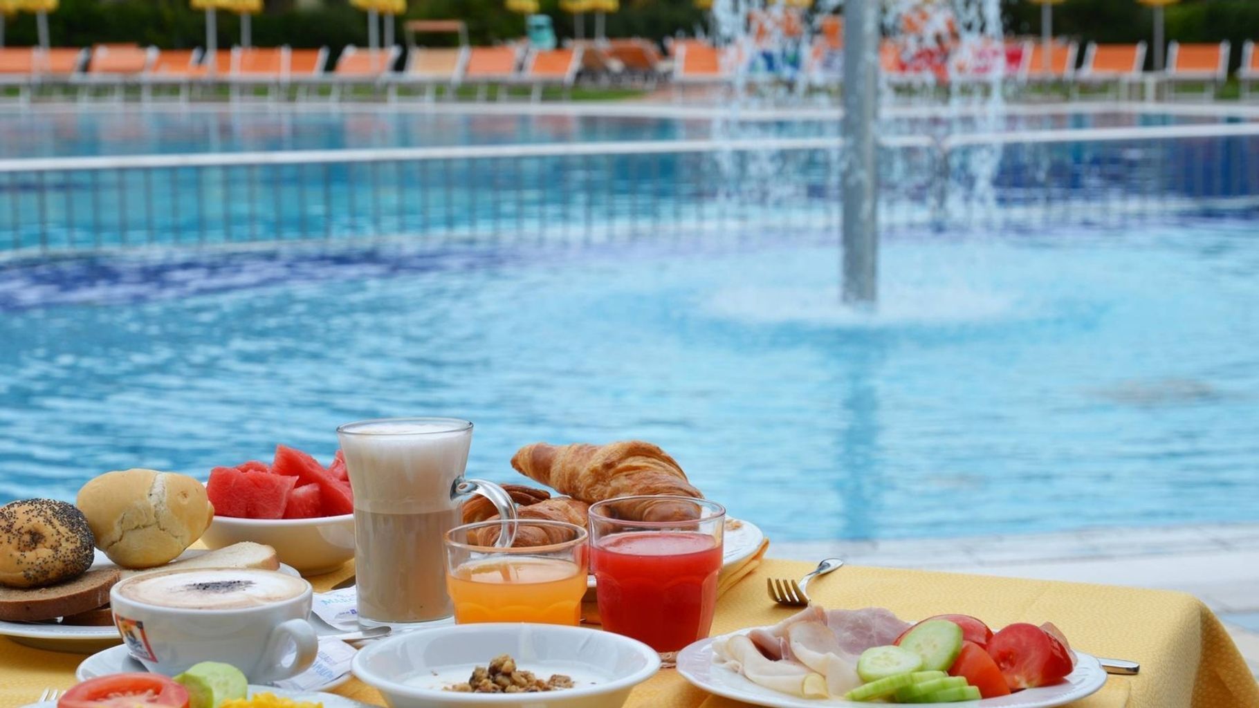 A breakfast setting with a pool view, including croissants, fruit, and beverages.