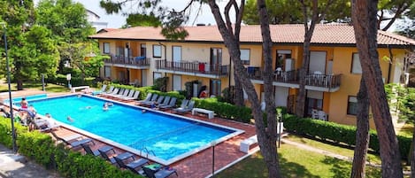 A swimming pool with lounge chairs, surrounded by trees and a building with balconies.