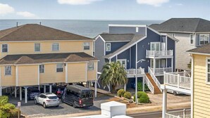 A coastal residential area with multi-story buildings, a parking lot, and a view of the ocean. - The Penalty Box- 5 bed, 5+ bath with putting green, corn hole, & hammock swing. (Ocean Isle Beach)