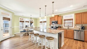 A spacious kitchen with a large island, wooden cabinets, and stainless steel appliances. - The Penalty Box- 5 bed, 5+ bath with putting green, corn hole, & hammock swing. (Ocean Isle Beach)