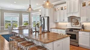 A spacious kitchen with white cabinetry, a large island with bar stools, stainless steel appliances, and pendant lighting.