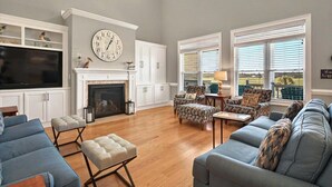 A living room with a fireplace, a large clock, and a television.