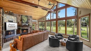 A spacious living area with a stone fireplace, leather sofa, and large windows offering a view of the outdoors.