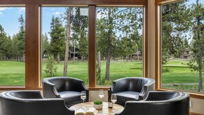 A room with large windows, two black leather chairs, a round wooden table, and a view of a golf course.