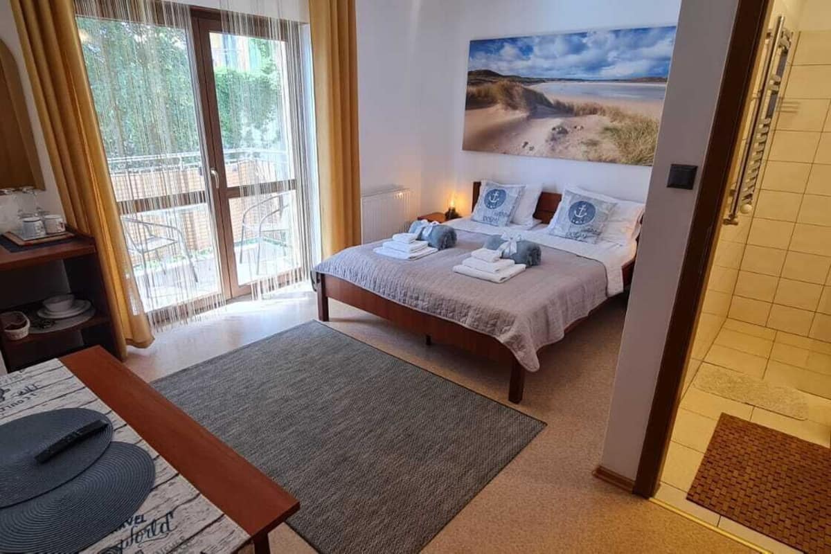 Ein Schlafzimmer mit Bett, Schreibtisch, Stuhl, einem Fenster mit Vorhängen, einem Bild an der Wand und einer Duschkabine.