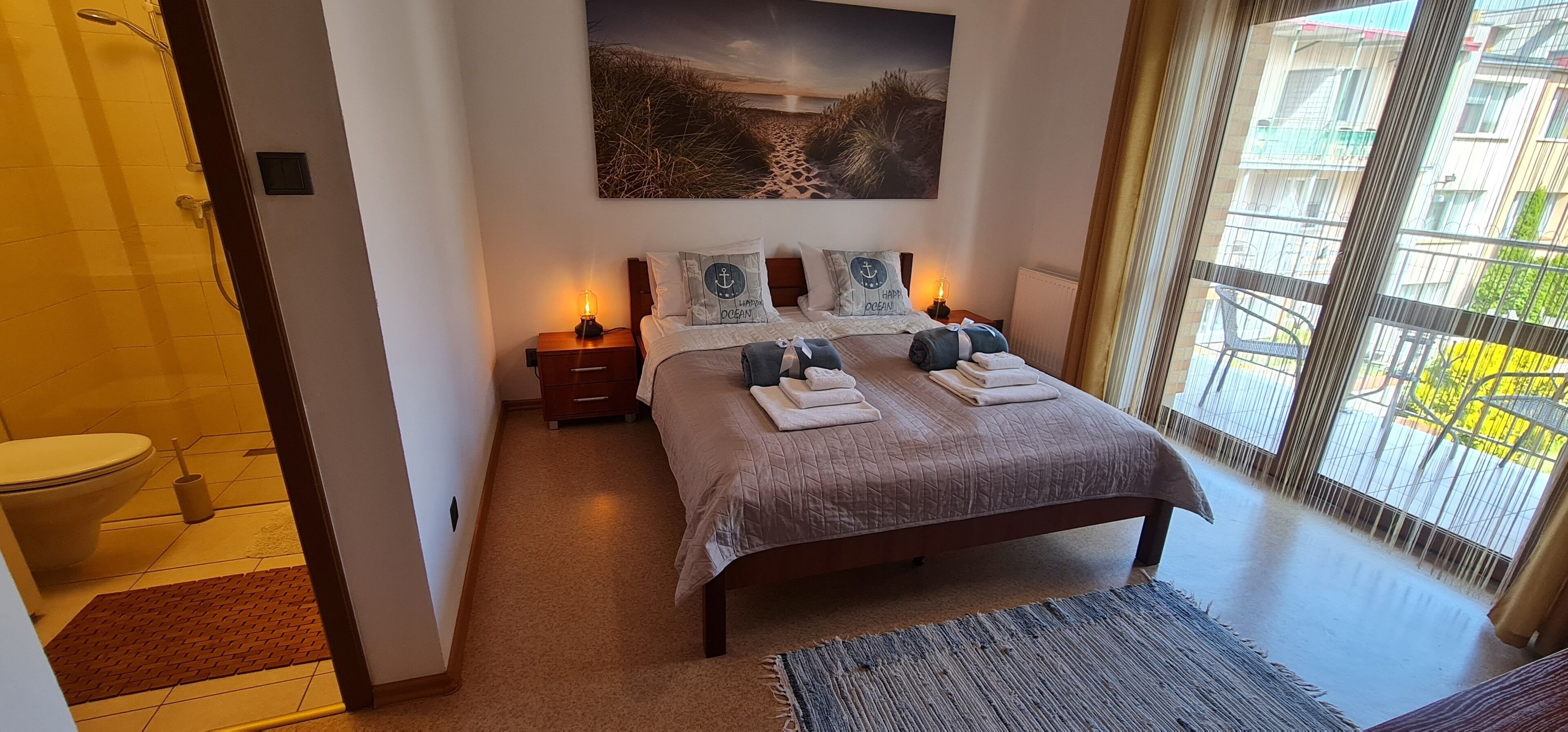 Ein Schlafzimmer mit Bett, Nachttischen, einem Wandbild und Blick ins Freie.