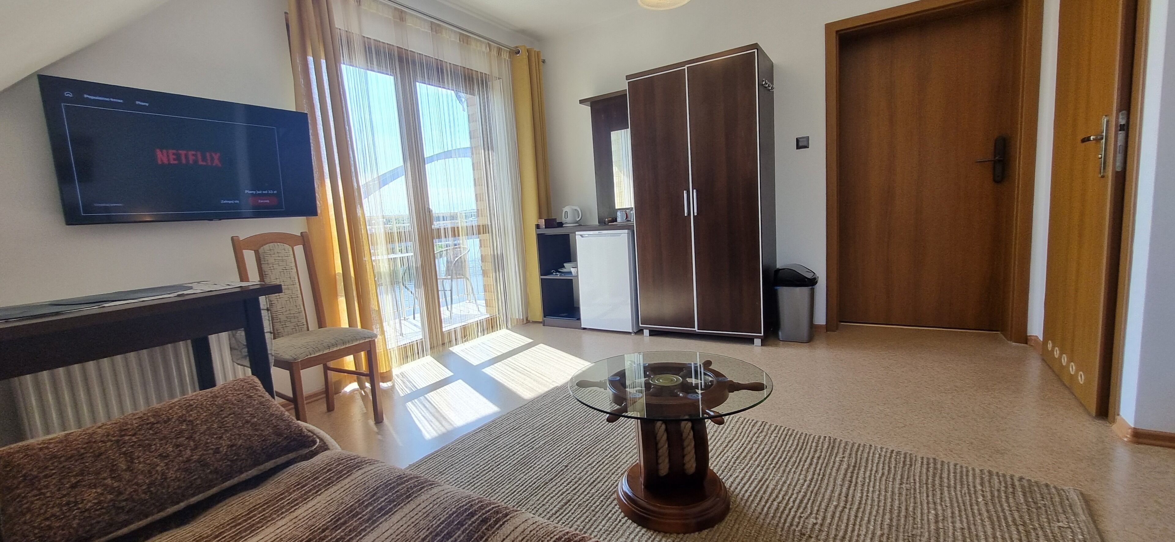 A modern living room with a flat-screen TV, a glass coffee table, a sofa, and a sliding glass door leading to a balcony.