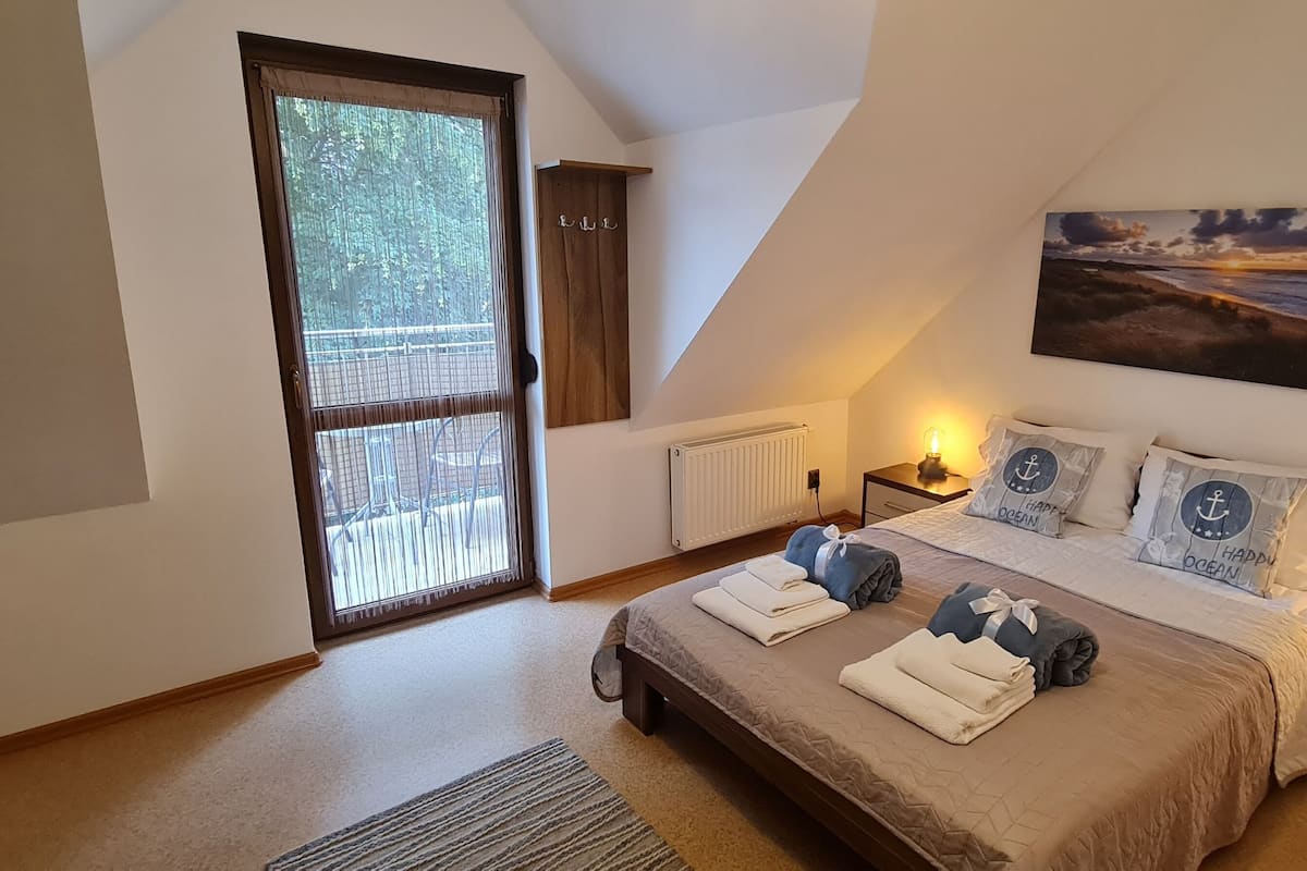 Ein Schlafzimmer mit einem großen Bett, Blick ins Freie durch eine Schiebetür, einem Bild an der Wand und einem Nachttisch mit Lampe.