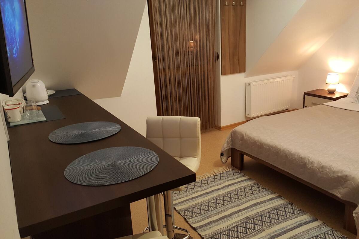 Ein Hotelzimmer mit einem Bett, einem Schreibtisch mit zwei runden Unterlagen, einem Stuhl, einem Fernseher, einer Lampe und einem Bild an der Wand.