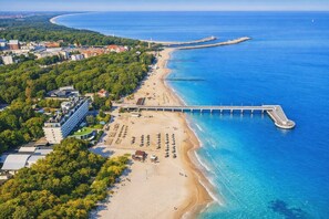 An aerial view of a coastal area with a beach, a pier, and buildings. - Villa Kapitańska (Kolobrzeg)