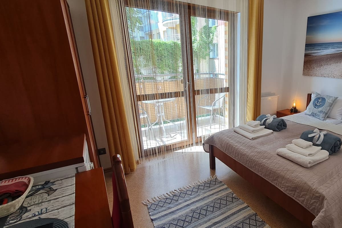 Ein Schlafzimmer mit Bett, Nachttischen, einem Bild und Blick ins Freie.