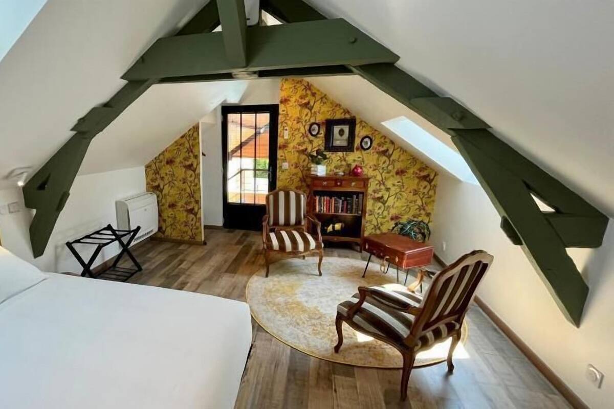 A bedroom with a bed, a chair, a small table, a bookshelf, and a door leading to an outdoor area.