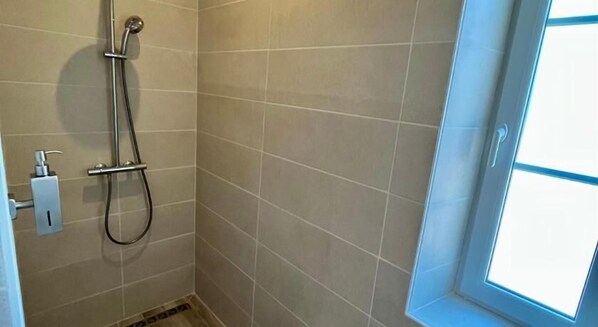 A small, tiled shower room with a glass door and a visible hand soap dispenser.