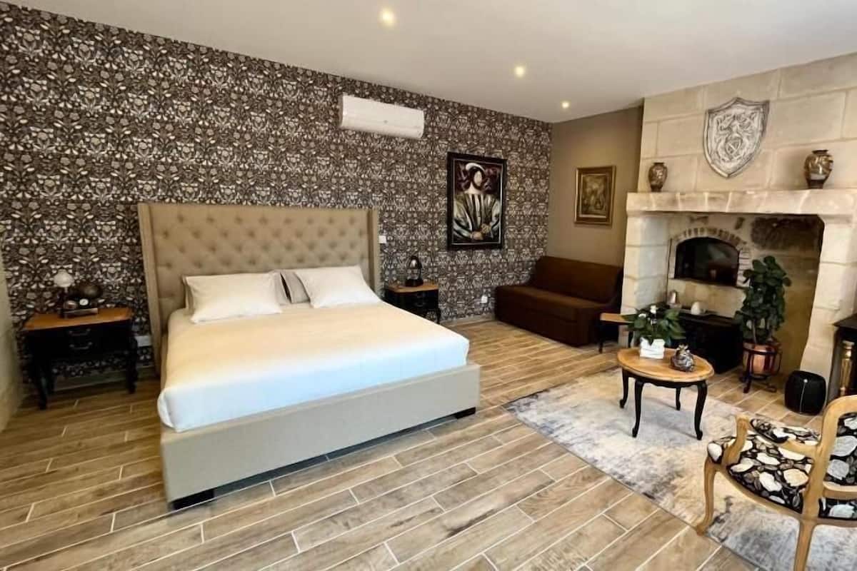 A bedroom with a large bed, a sofa, a small table, and a fireplace.
