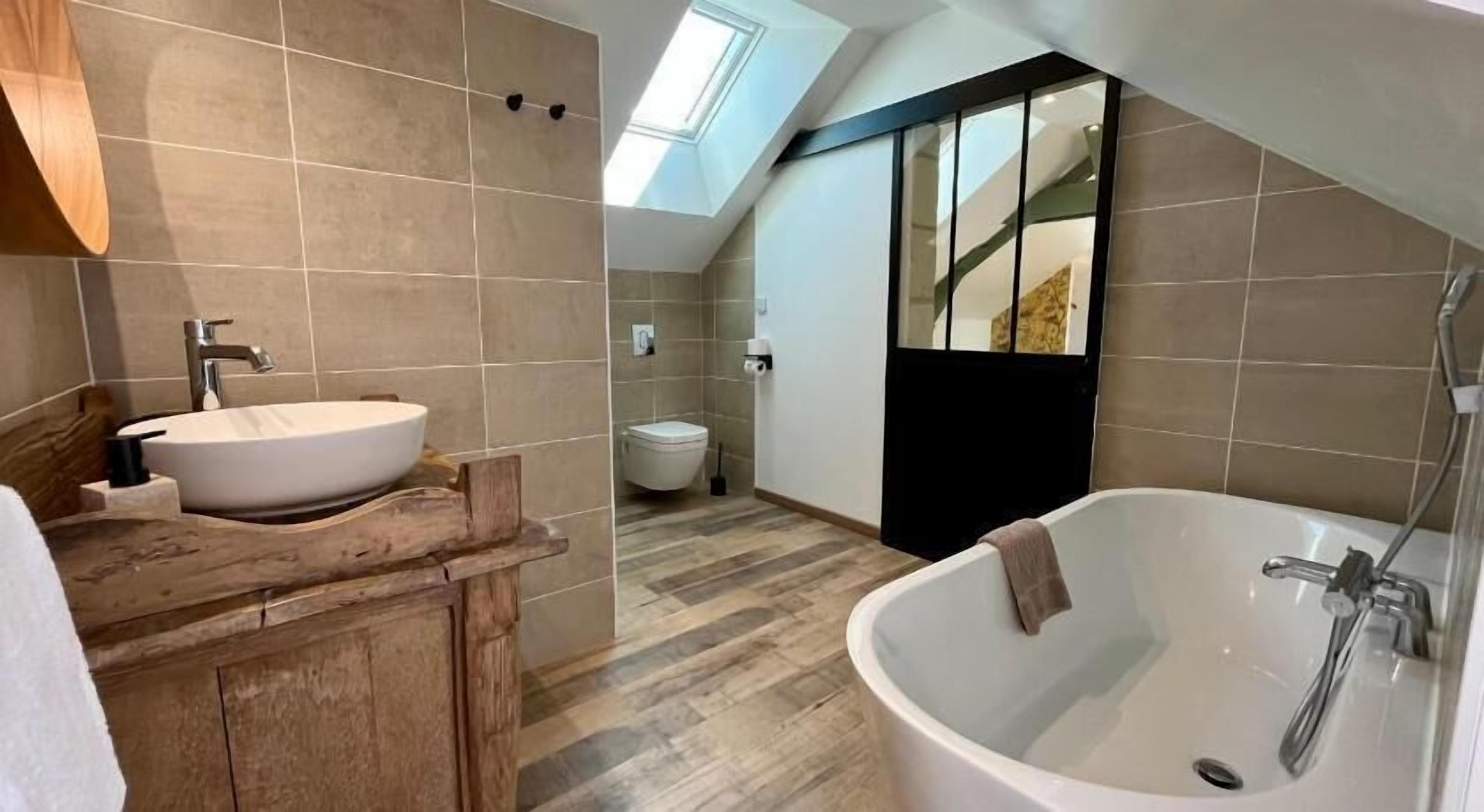 A modern bathroom with a skylight, a freestanding bathtub, and a wooden vanity.