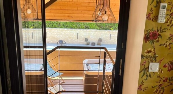 A balcony with a wooden railing, two cushioned seating areas, and hanging pendant lights. - Cave Auger La Maison d'Hotes (Restigne)
