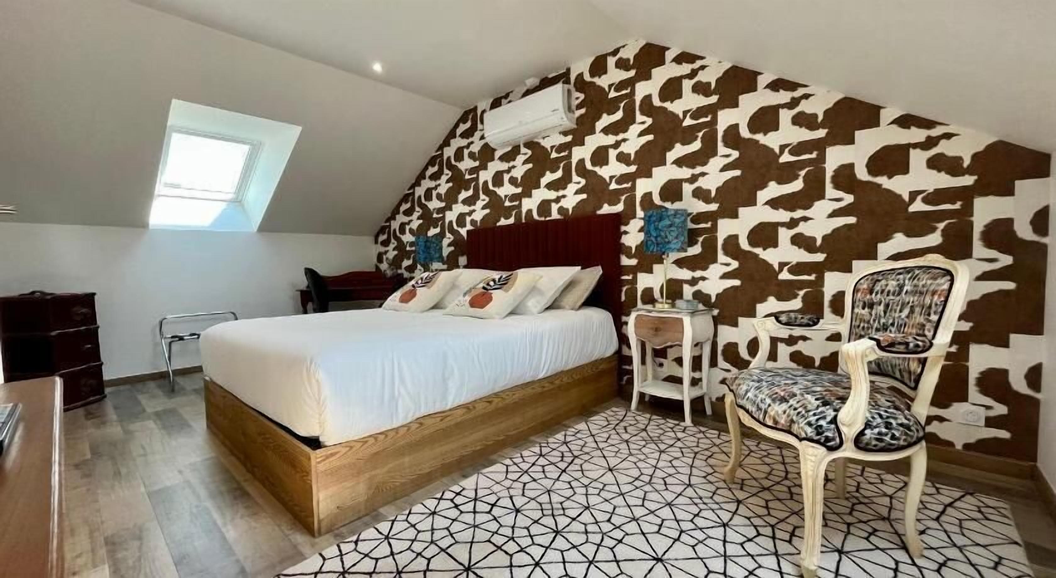 A bedroom with a bed, a chair, a desk, and a patterned wall.