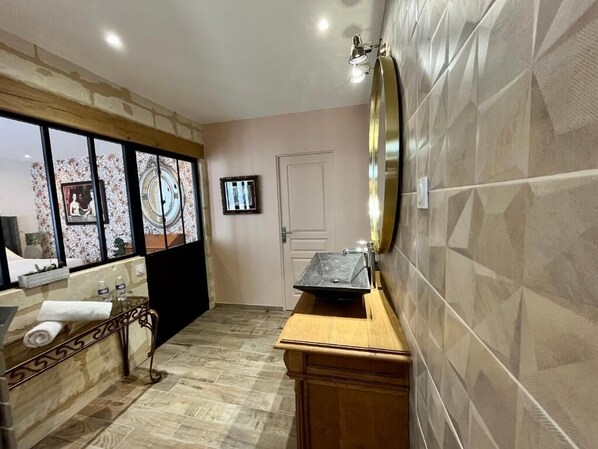 Une salle de bain avec un meuble-lavabo en bois, un grand miroir et un mur recouvert de carreaux.