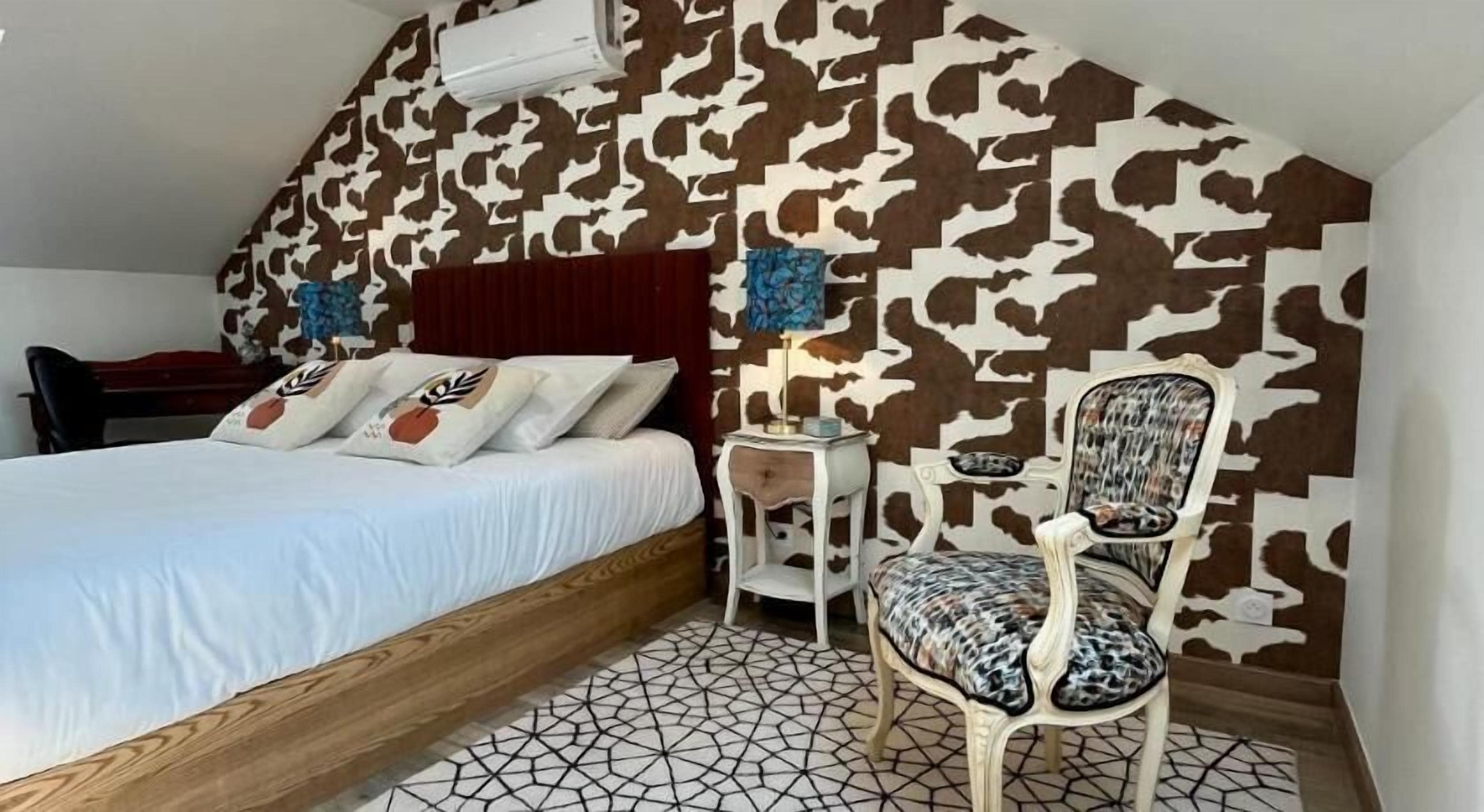 A bedroom with a bed, a chair, a nightstand, and a wall with a camouflage pattern.