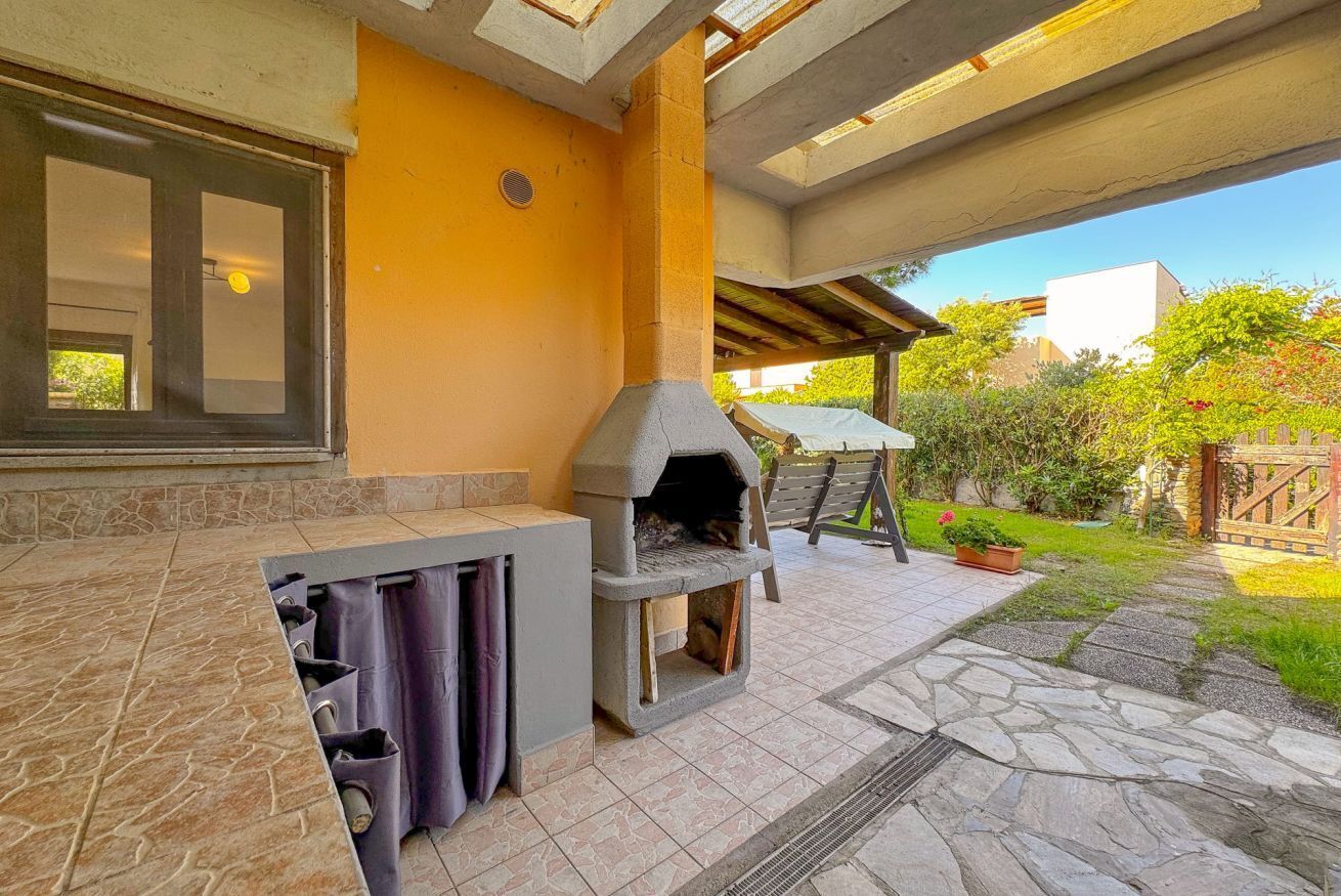 Zona de cocina al aire libre con horno de piedra, ventana y patio con baldosas de piedra y vistas a un jardín.