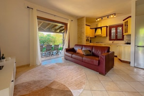 A living room with a leather sofa, a kitchen with wooden cabinets, and a sliding glass door leading to an outdoor area.