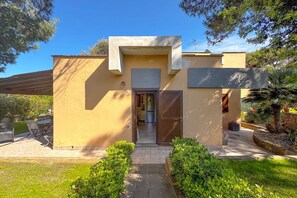 Un edificio moderno con fachada color beige, una puerta de madera y un pequeño patio con mobiliario exterior.