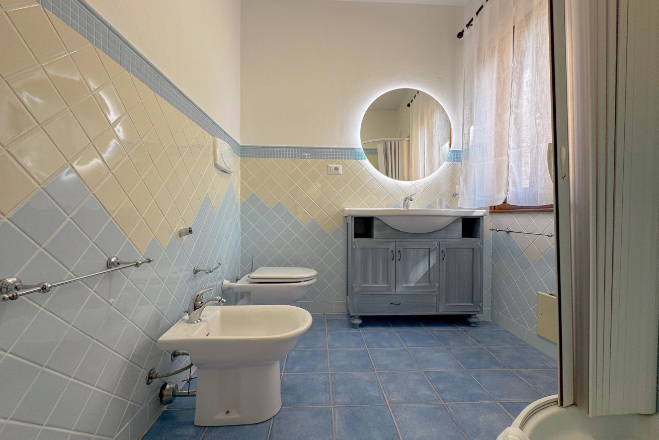 Ein Badezimmer mit Toilette, Bidet und Waschbecken, mit blauen und beigefarbenen Fliesen und einem Spiegel über dem Waschbecken.